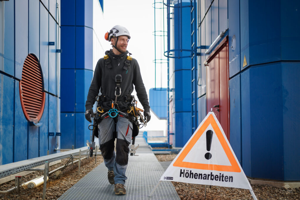 Benjamin Liebert auf einer Baustelle vor einem Warnschild auf dem Steht Höhenarbeit